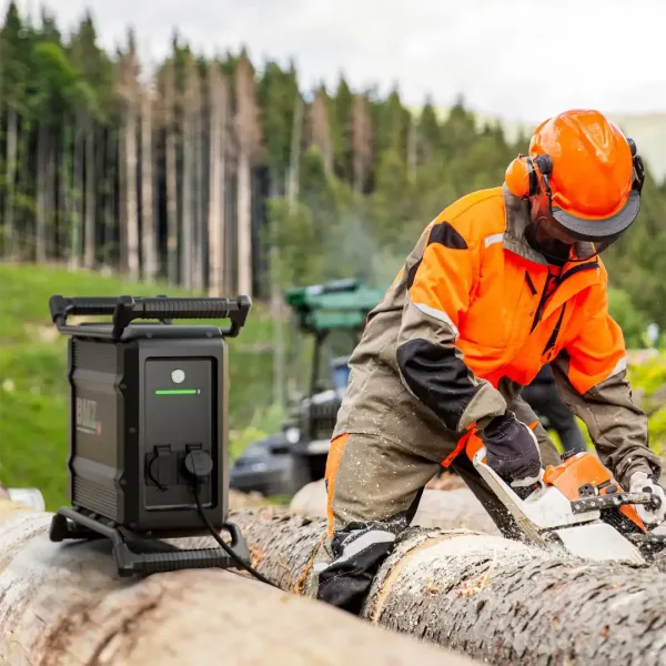 En arbeider som bruker BMZ Power2GO Work med en Stihl kjedesag BMZ Power2Go Work gir kraft til kappsag på byggeplass Mobil strømforsyning til kappsag ved utendørs prosjekter